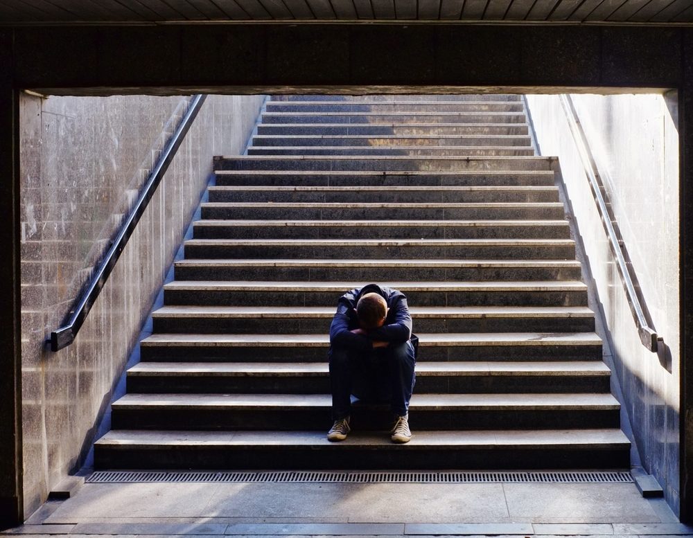 Depressed man with head down sitting on the stairs